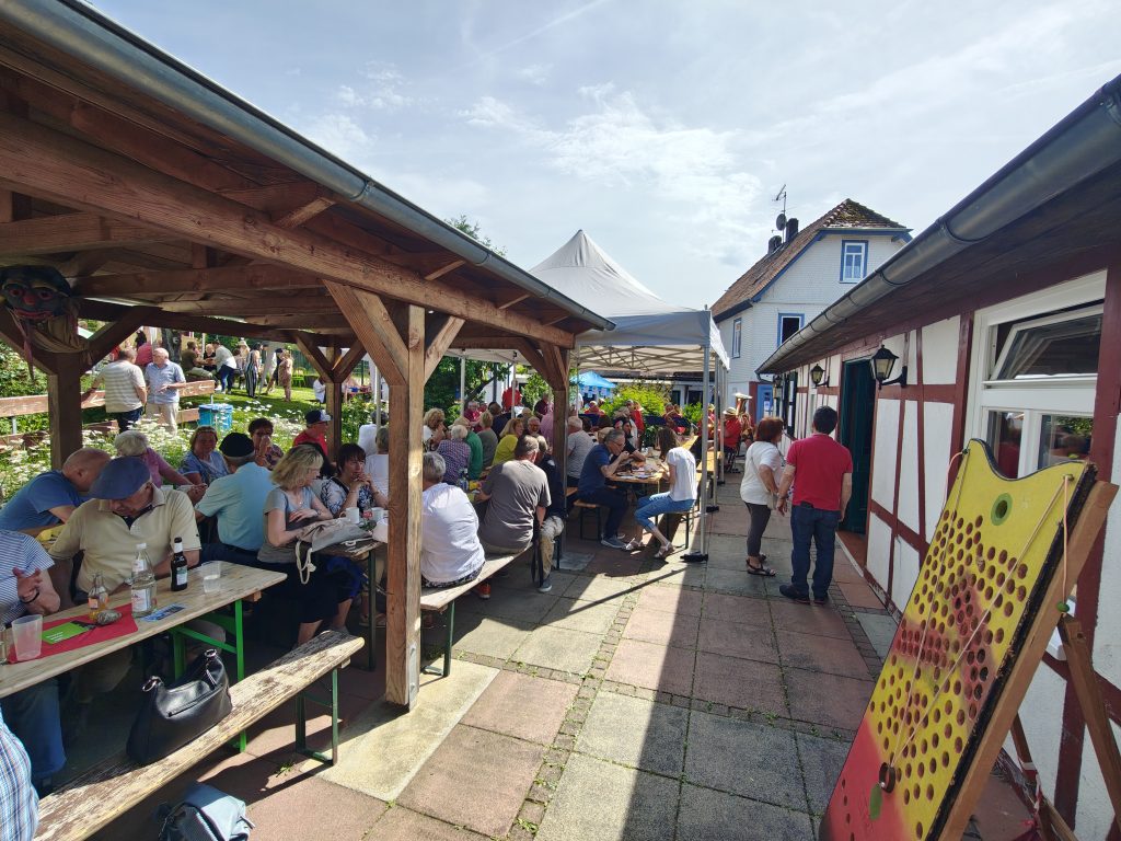 Bei strahlendem Sonnenschein sitzen die Besucher im großen Garten und Hof des „Selbstversorgerhauses Lützel“ beisammen und lauschen den Klängen von „BrützelBrass“. (Foto: DF)